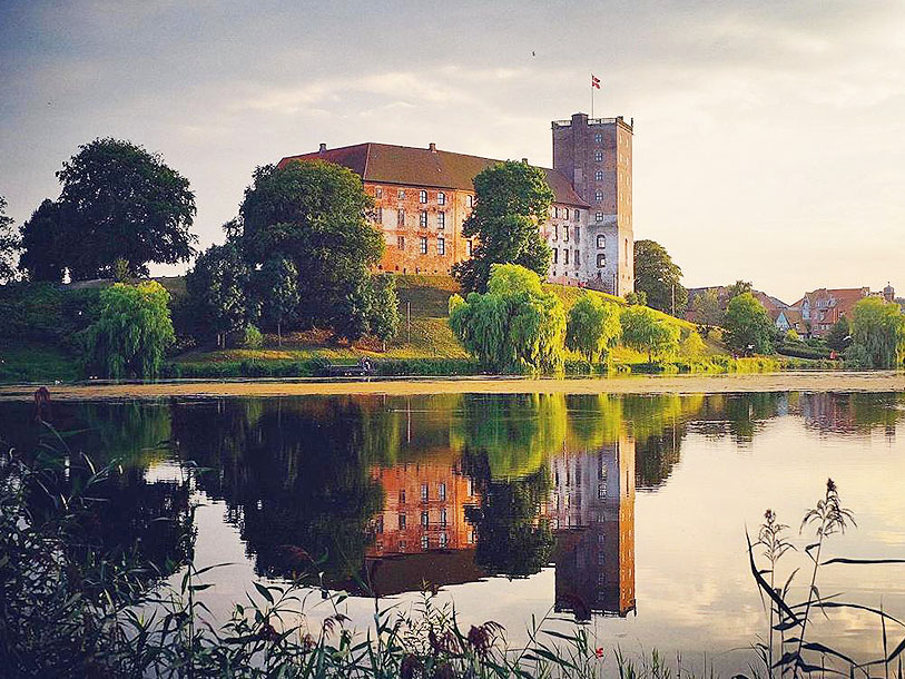 Se Koldinghus, Jyllands sista kungaborg, som speglar sig i slottsjön i Koldings centrum